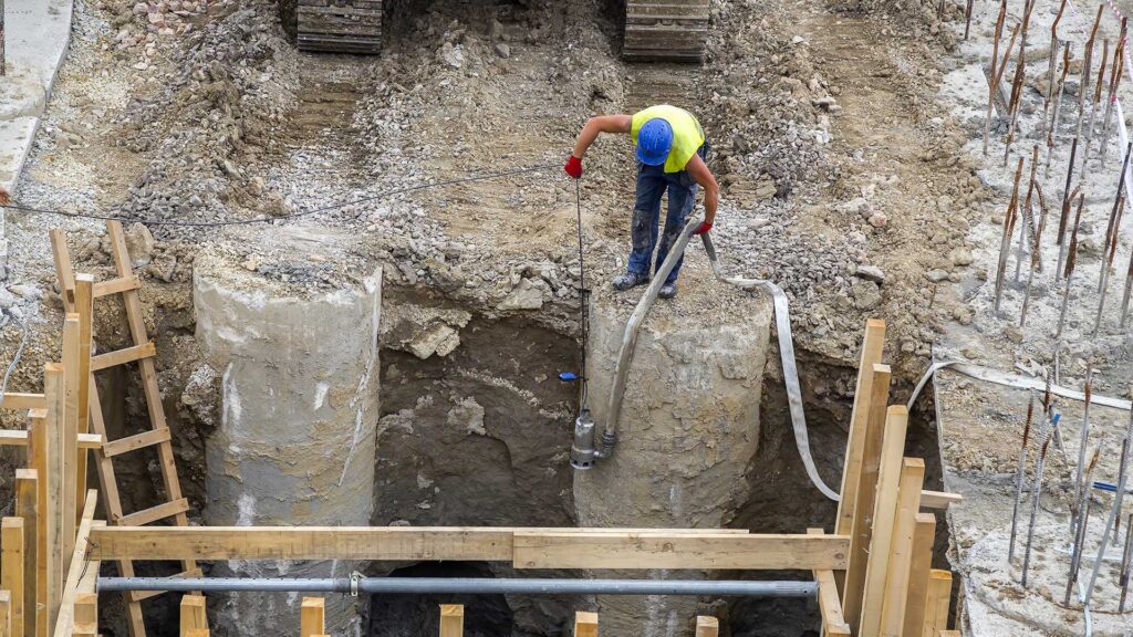 Construction worker lowering a water pump into a hole