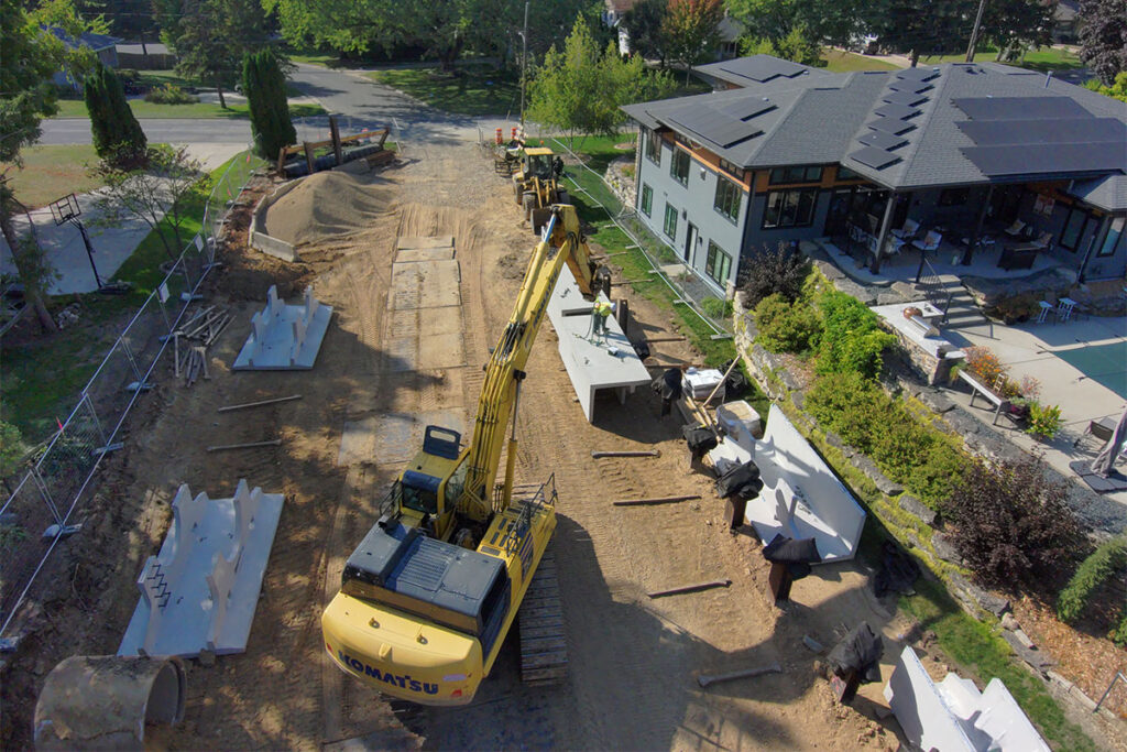 Excavator placing precast concrete structures along a residential construction site